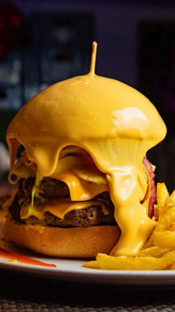 Hamburguesa bañada en queso cheddar servida con papas fritas en En Alturas Café Bistró Bar, Mérida.