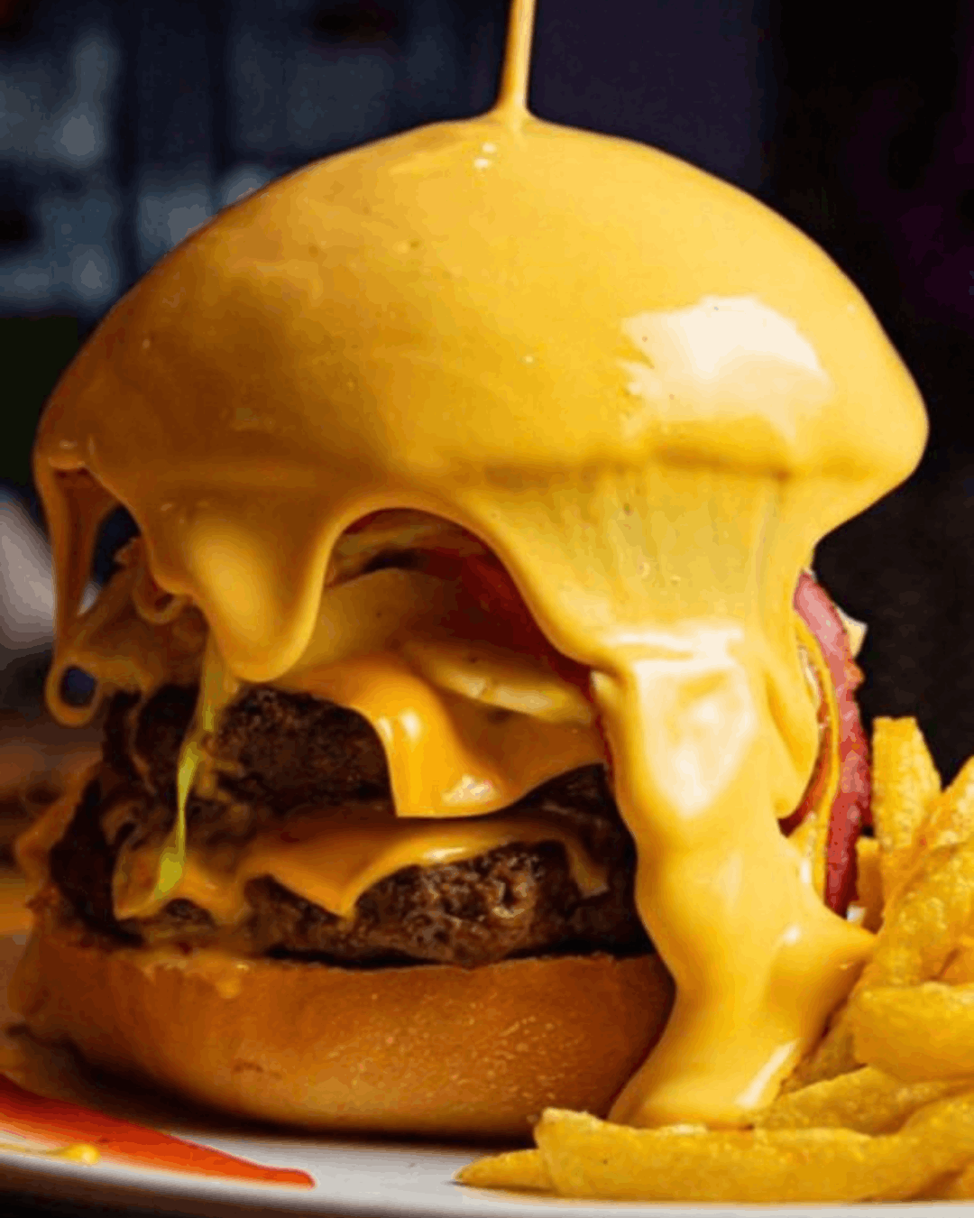 Hamburguesa bañada en queso cheddar servida con papas fritas en En Alturas Café Bistró Bar, Mérida.