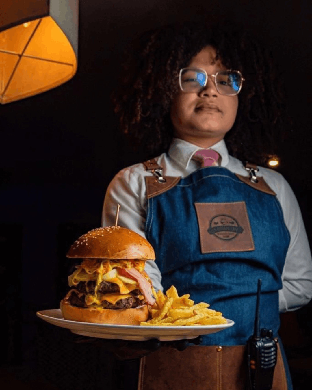 Mesero sirviendo una hamburguesa con papas fritas en En Alturas Café, Mérida.