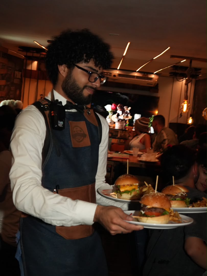 Mesero de En Alturas Café Bistró Bar sirviendo hamburguesas a turistas en Mérida.